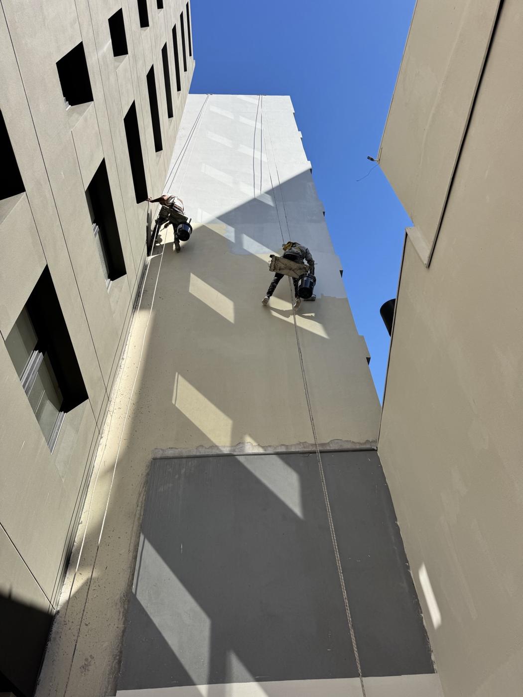 Dos pintores en silleta sobre una fachada blanca